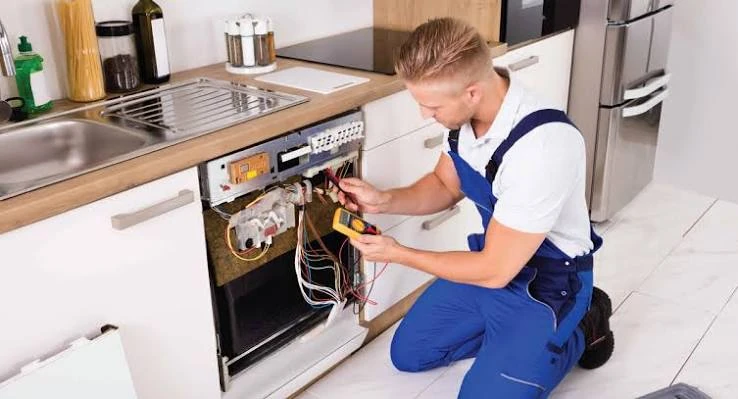 Technician testing the exposed controls of a dishwasher with a multimeter