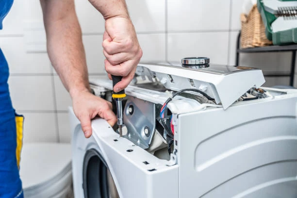 Close-up of a technician removing a washing machine top panel with a screwdriver
